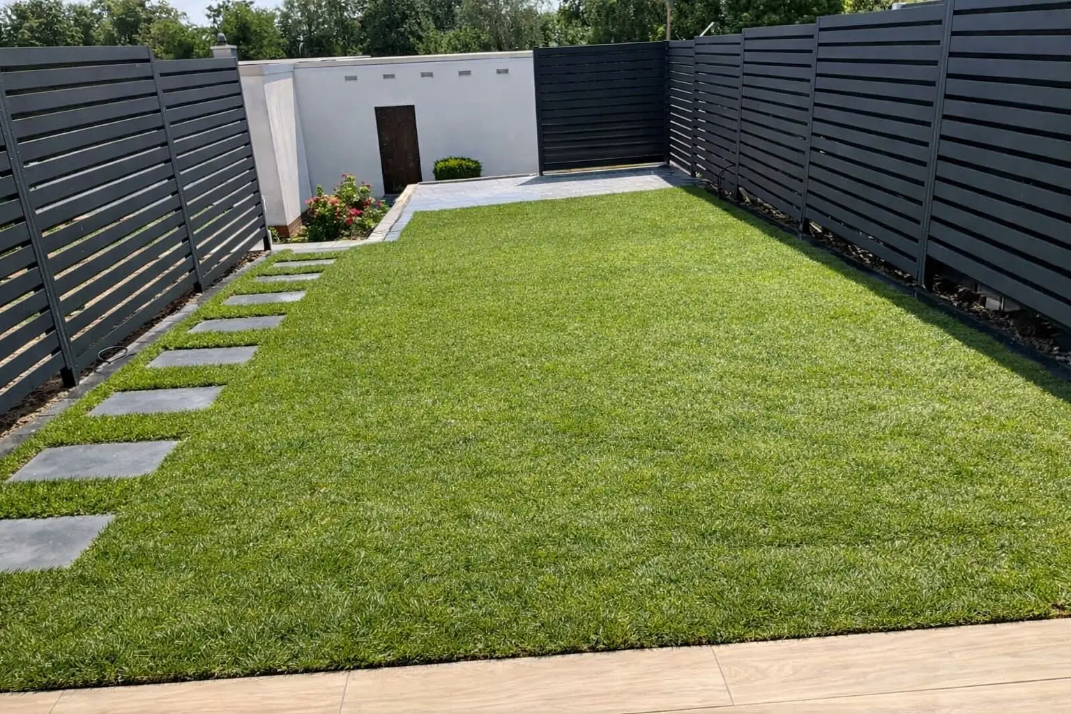 Fertiger Garten mit Rollrasen, Trittplatten und weißer Gartenmauer