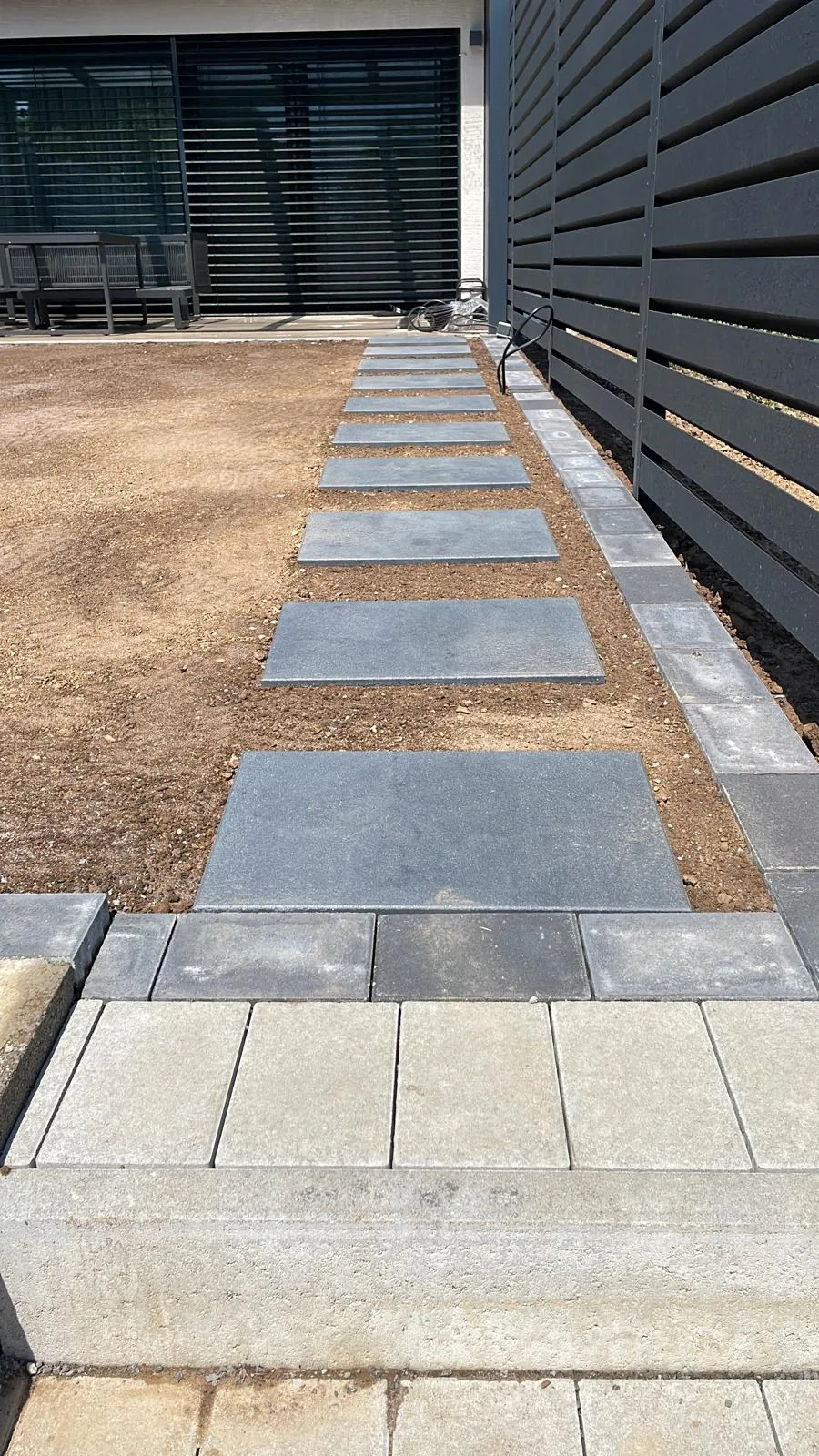 Trittplattenweg aus dunklen Platten entlang eines modernen Sichtschutzzauns