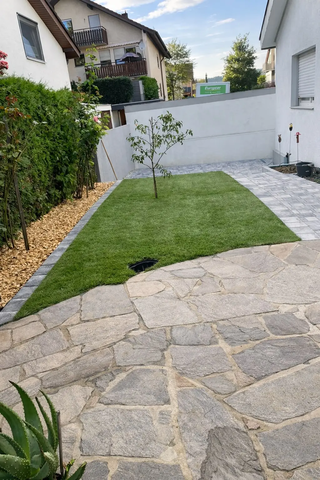 Weg aus Naturstein-Polygonalplatten neben frischem Rasen und weißer Mauer