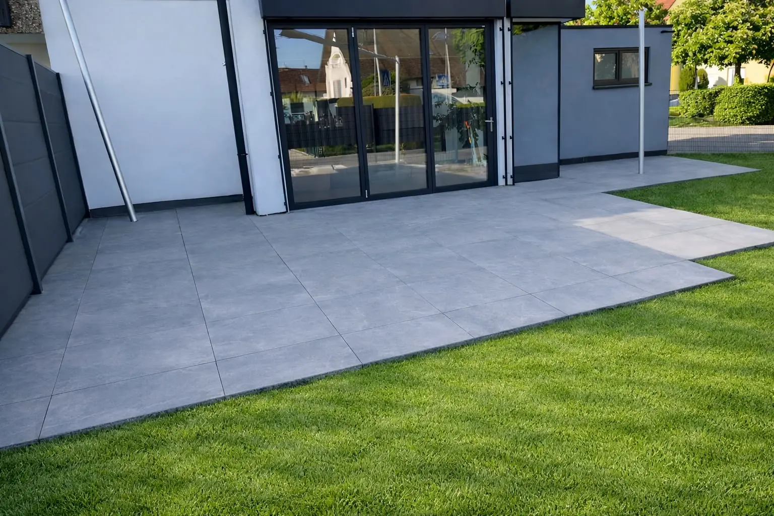 Große moderne Terrasse aus Feinsteinzeug mit frisch verlegtem Rollrasen am Neubau
